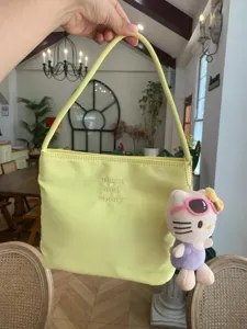 Yellow nylon shoulder bag detail, cute embroidered lettering and cartoon cat plush charm pendant.