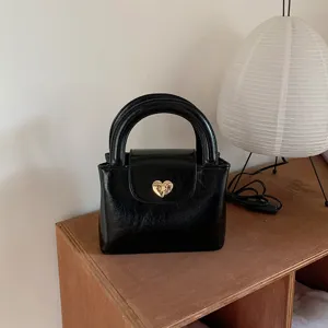 Black leather handbag with gold heart lock on wooden table, detailed view of textured bag.