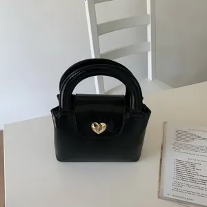 Close-up detail of black patent leather handbag with gold heart-shaped turn-lock closure.