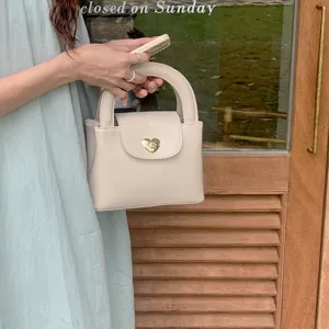 Beige handbag detail shot showcasing the elegant heart-shaped lock and curved handle.
