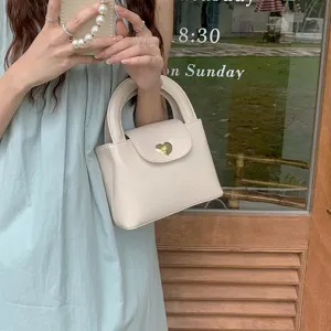 Detail shot of cream white mini handbag featuring cute golden heart clasp and sturdy handle.