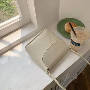 Detail view of a minimalist cream shoulder bag placed by a sunny window with props.