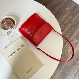Detail shot of a minimalist red glossy shoulder bag, retro flap bucket bag design for women commuting.