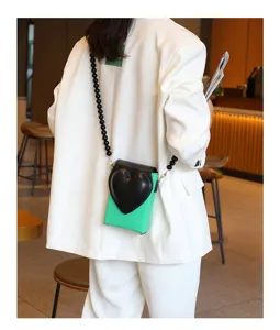 Nahaufnahme einer trendigen grünen Mini-Handy-Tasche mit schwarzer Herzklappe und Perlenkette.