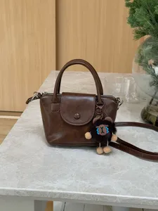 Stylish brown mini handbag for women, versatile crossbody bucket bag with cute bear pendant.