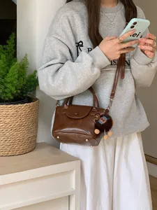 Brown PU leather top-handle crossbody bucket bag detail showing texture and plush charm.