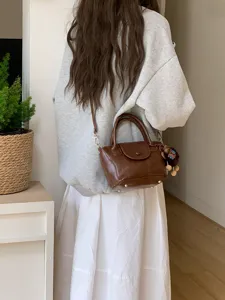 Detail view of a stylish brown leather crossbody bucket bag worn by a model in casual outfit.