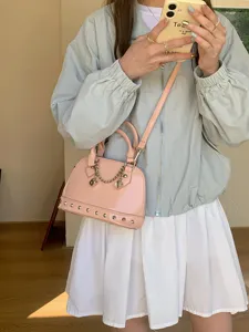 Stylish pink patent leather shell crossbody handbag with metal studs and chain accessory for women.