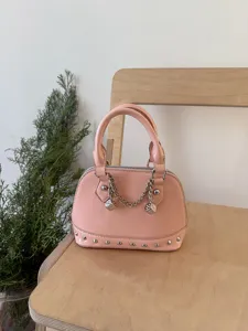 Chic pink patent leather dome shoulder bag with chain dice charms and studded bottom detail.