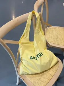 Gelbe Canvas-Tragetasche für Damen, leichte Pendler-Schultertasche mit grünem Aufdruck.