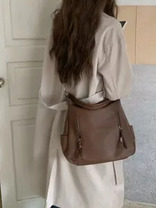 Detailed lifestyle shot of a brown leather slouchy shoulder bag worn with beige trench.