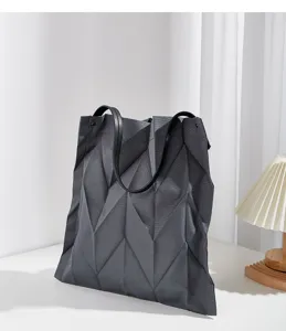 Detailed view of a dark grey geometric pleated tote bag on desk with lamp, large capacity.