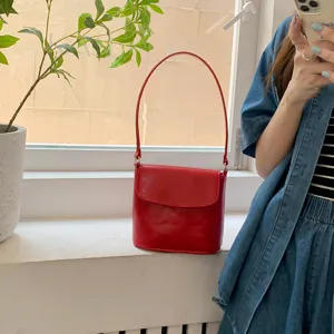 Red patent leather bucket bag on windowsill, chic glossy minimalist shoulder handbag detail.