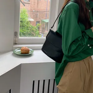 Detailed view of black minimalist leather shoulder bag, everyday casual style in cozy interior.