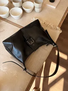 Detailed shot of retro black soft leather underarm shoulder bag with metal buckle in cafe setting