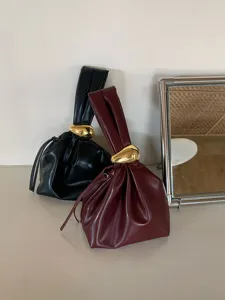 Λεπτομερής λήψη κομψών πτυχωτών τσαντών σύννεφο σε μαύρο και μπορντό με χρυσό κόμπο.