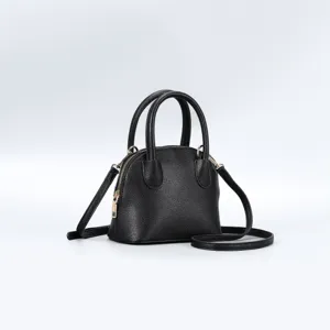 Black leather dome handbag detail view, showing fine texture, metal zipper and sturdy dual top handles.