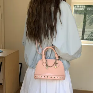 Stylish pink patent leather shell crossbody bag with metal chain and bottom rivets for women.