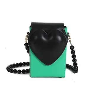 Schicke grüne Mini Handytasche als Umhängetasche mit schwarzem Herz-Deckel und Perlenkette.