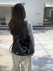 Detailed shot of a black soft leather hobo shoulder bag with metal buckle in a street scene.