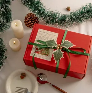 Scatola regalo di Natale rossa con nastro verde e decorazione di bacche di agrifoglio festive