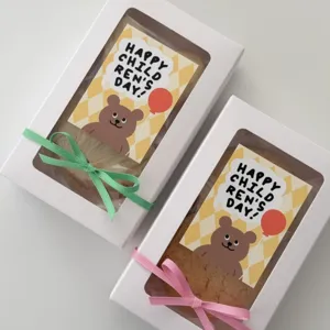 Nahaufnahme von weißen Geschenkboxen mit Sichtfenster, süßen Bärenstickern und bunten Schleifen.