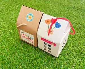 Detailaufnahme von DIY-Haus-Geschenkboxen aus Papier mit niedlichen Stickern auf Rasen.