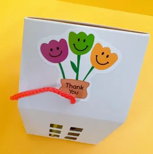 Geschenkverpackung mit bunten Tulpen-Lächeln-Aufkleber und Griff, ideal für Partytisch.