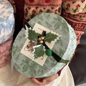 Scatola regalo rotonda di Natale con motivo di alberi, nastro verde e decorazione natalizia di bacche