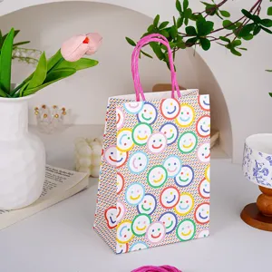 Vista detallada de la bolsa de regalo de papel colorida con caras sonrientes y asas rosas.