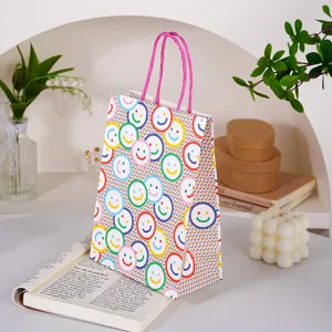 Bolsa de regalo de papel con diseño de caras sonrientes coloridas, vista de detalle con asas rosas.