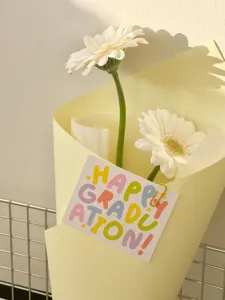 Nahaufnahme einer Abschluss-Grußkarte mit bunten Morandi-Buchstaben am Blumenstrauß.