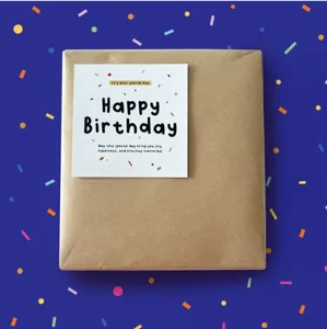 Primer plano de una tarjeta de felicitación de cumpleaños cuadrada con confeti en caja marrón.