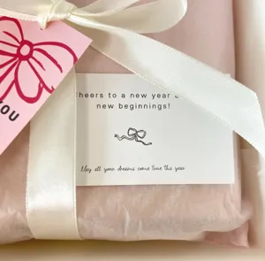 Gift wrapping detail showing pink tissue paper, white ribbon bow, and thank you card.
