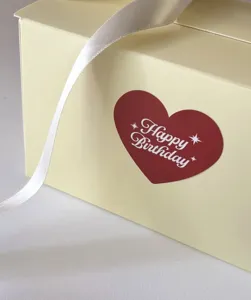 Gros plan détaillé d'une élégante boîte cadeau jaune avec autocollant cœur et ruban blanc.