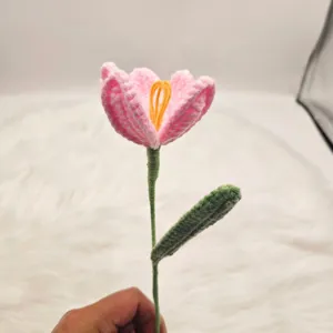 Handmade crochet tulip flower detail shot, pink knitted bloom with green stem and leaf decor.