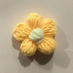 Detailed close-up of handmade crochet wool puff flower, yellow petal clothing accessory.