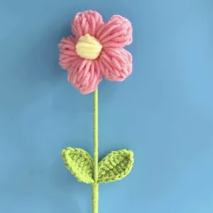 Close-up detail of handmade crochet flower with pink petals and green leaves, yarn art.