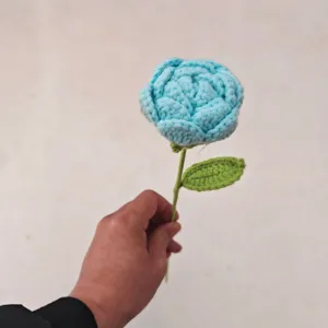 Hand holding handmade crochet blue rose detail close up view showing texture and fine craft