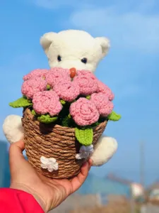 Close-up detail of handmade crochet pink rose bouquet in woven basket with cute white plush bear.