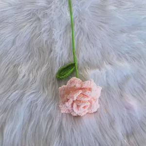 Handmade crochet pink rose flower detail view, green stem with single leaf, wool knit craft decor.