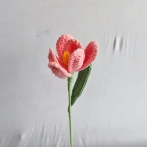 Detailed close-up view of handmade crochet pink flower with green leaf and stem decor