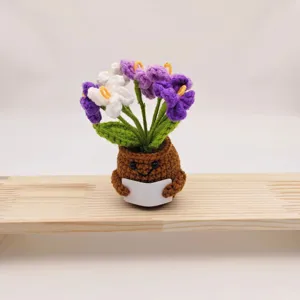 Close-up detail of cute handmade crochet forget-me-not potted plant with smiling pot design.