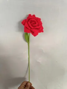 Detailed shot of a handmade crochet red rose with green stem and leaf, delicate wool craft.