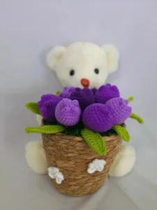 Handmade crochet white teddy bear holding a purple tulip flower basket, detailed crafting.