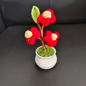 Handmade crochet potted flower detail, showing red yarn blooms and white ceramic pot.