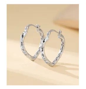 Gros plan détaillé de boucles d'oreilles créoles argentées en forme de cœur texturé.