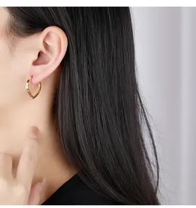 Gros plan détaillé de boucles d'oreilles créoles cœur texturées portées, éclat métallique.