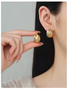 Close-up view of gold chunky braided C-hoop earrings worn on ear and held in hand.