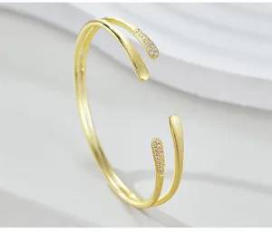 Primer plano detallado de pulsera brazalete abierta de doble banda dorada con cristales.